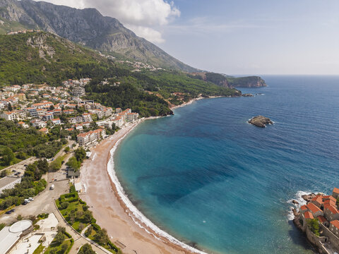 Aerial view of Sveti Stefan, featuring terracotta-roofed buildings on an islet connected to the mainland, surrounded by turquoise waters in Sveti Stefan, Budva Municipality, Montenegro.