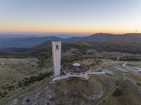 Aerial view of the abandoned Buzludzha Monument with its iconic tower and saucer-shaped structure set against the rolling hills and mountains of Stara Zagora, Bulgaria.