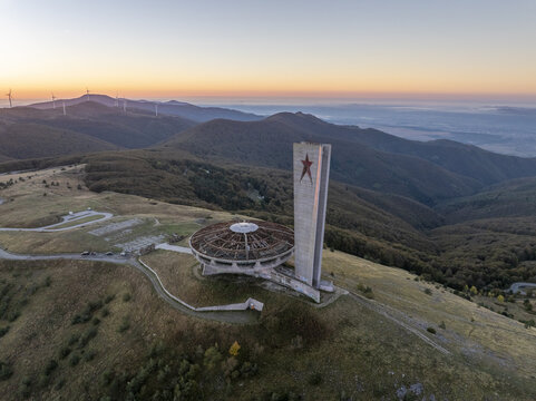 Aerial view of the abandoned Buzludzha Monument perched on a mountain peak at sunset with wind turbines in the distance in Stara Zagora, Bulgaria.
