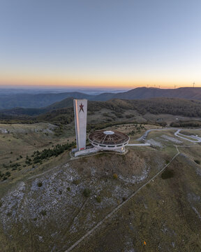 Aerial view of the Buzludzha Monument, a brutalist saucer-shaped structure with a tall tower featuring a red star, situated on a mountain peak in Stara Zagora, Bulgaria.