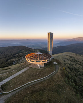 Aerial view of the abandoned brutalist Buzludzha Monument atop a mountain peak at sunset, with rolling hills and clear sky in Stara Zagora, Bulgaria.