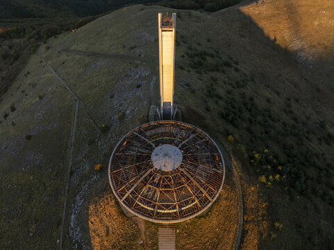 Aerial view of the Buzludzha Monument, a brutalist structure with a circular roof and tall tower, situated on a mountain peak in Stara Zagora, Bulgaria.