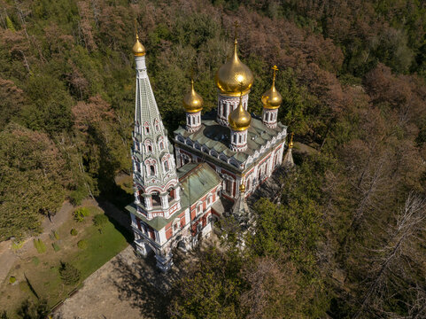 Aerial view of Shipka Memorial Church with its golden domes and tall bell tower, surrounded by dense forest in autumn in Shipka, Stara Zagora, Bulgaria.