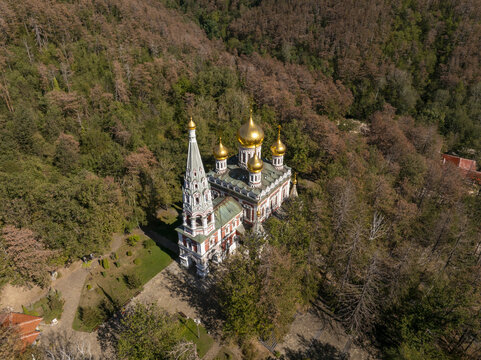 Aerial view of the Shipka Memorial Church with its distinctive golden domes and ornate bell tower nestled among the dense autumn forest in Shipka, Stara Zagora, Bulgaria.