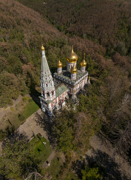 Aerial view of the Shipka Memorial Church with its distinctive golden domes and tall bell tower nestled within a dense forest in Shipka, Stara Zagora, Bulgaria.