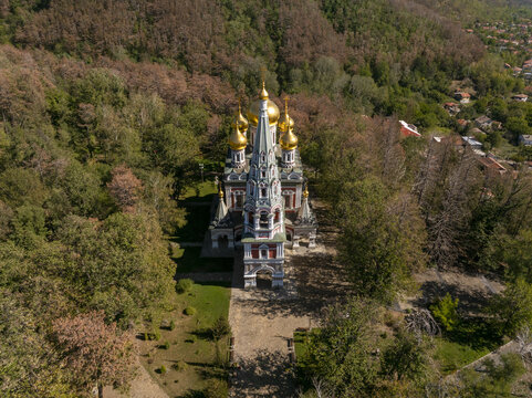 Aerial view of Shipka Memorial Church with its golden domes, surrounded by dense autumn forest in the mountains of Shipka, Stara Zagora, Bulgaria.