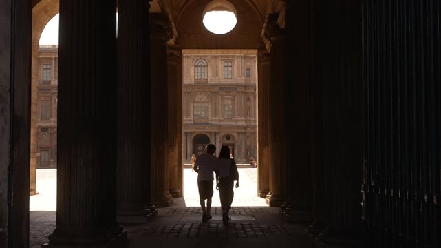 Two figures walking through a shadowed Paris palace passage