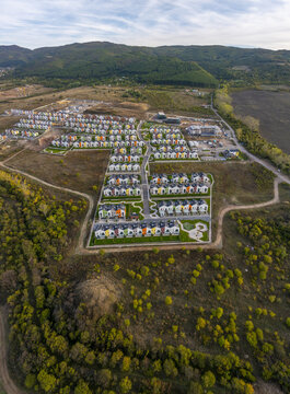 Aerial view of Residential Park Lozen featuring rows of modern colorful houses with green lawns and paved streets surrounded by autumn hills in Sofia, Sofia City Province, Bulgaria.