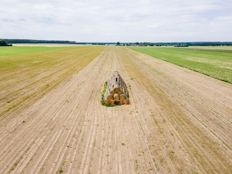 Aerial view of a person standing on a large stack of hay bales in a vast agricultural field in Poland.