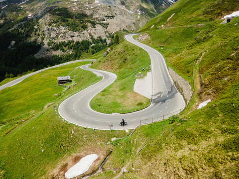 Aerial view of the Grossglockner High Alpine Road winding through lush green mountain slopes with a lone cyclist riding along the asphalt in Zell am See District, Salzburg, Austria.