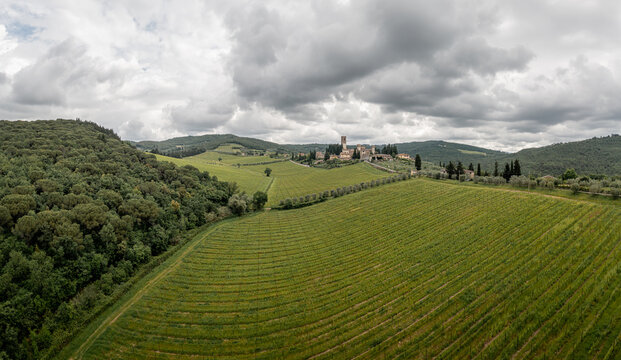 Aerial view of the village of Passignano nestled among rolling hills and lush green vineyards under a cloudy sky in Passignano, Toscana, Italy.