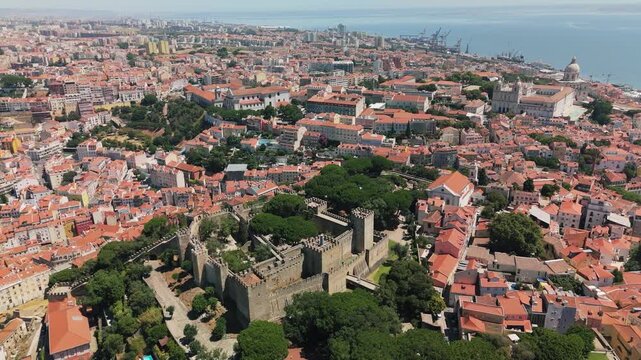 Aerial view of the historic Castelo de Sao Jorge surrounded by dense red-tiled rooftops and urban architecture in Lisbon, Portugal.