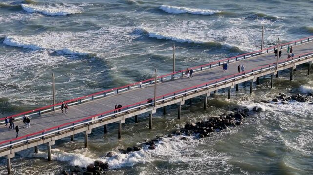 Aerial view of Palanga Pier with people walking along the wooden structure above the crashing waves of the Baltic Sea in Palanga, Klaipeda County, Lithuania.