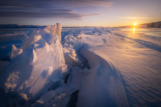 View of Lake Baikal with jagged ice formations and snow-covered surface under a golden sunset sky in Irkutsk, Irkutsk Oblast, Russia.