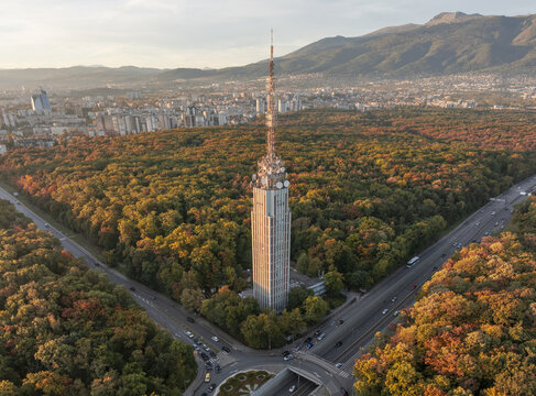 Aerial view of Sofia TV Tower surrounded by vibrant autumn forest, with city skyline and Vitosha mountain in the background Sofia, Sofia City Province, Bulgaria.