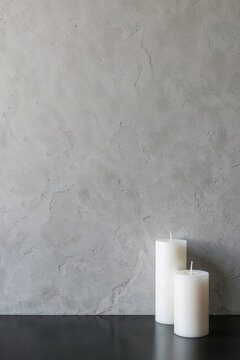 Two white unlit pillar candles on a dark table surface