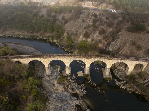 Aerial view of the historic stone railway bridge spanning a river in a hilly landscape with rocky banks and lush vegetation in Balabanovo, Kardzhali Province, Bulgaria.