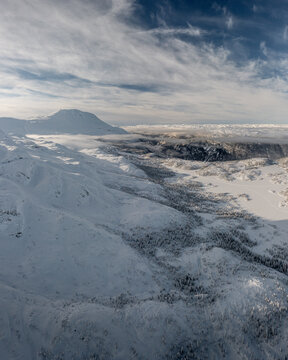 Aerial view of the snowy Gaustablikk Fjellresort area in the mountains, featuring vast snow-covered slopes, frozen lakes, and wispy clouds in Rjukan, Telemark, Norway.