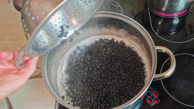 making homemade jam from black currant berries, pouring berries into boiling sugar syrup