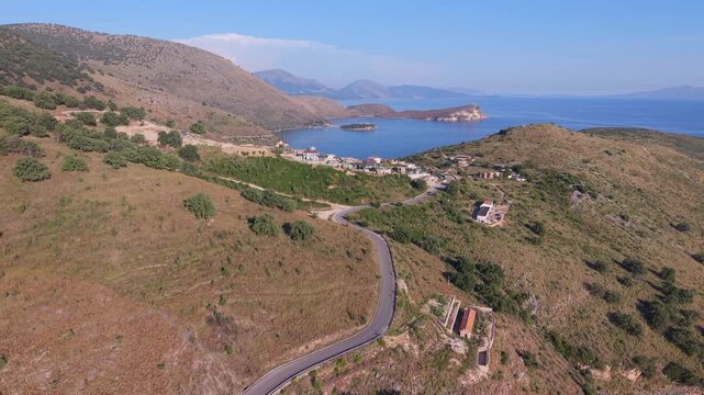 Aerial view of the winding coastal road leading to the bay with hills and blue sea in Porto Palermo, Qarku i Vlores, Albania.