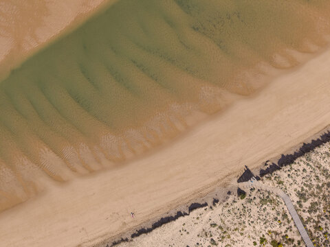 Aerial view of the sandy beach and clear water patterns at the coastline in Vila Nova de Milfontes, Beja District, Portugal.