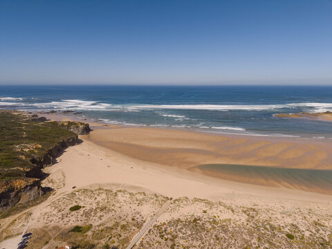Aerial view of the sandy coastline and rugged cliffs at Vila Nova de Milfontes beach, with the Atlantic Ocean meeting the shore in Vila Nova de Milfontes, Beja District, Portugal.