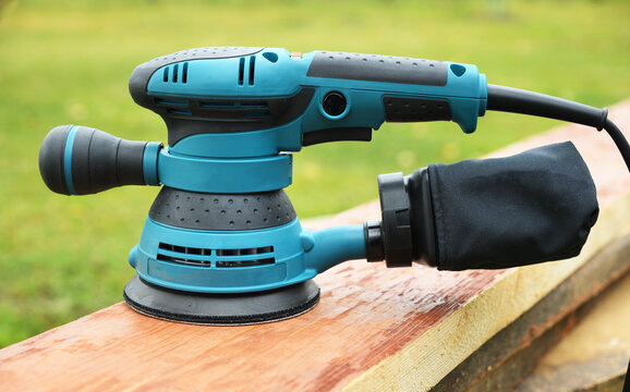  Close up of random orbit sander on wooden board outdoors.