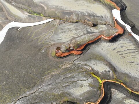 Aerial view of the volcanic landscape of Raudufossafjoll featuring vibrant orange iron deposits, dark basaltic terrain, and patches of snow in Hella, Rangarthing ytra, Iceland.