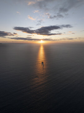 Aerial view of a small boat silhouetted on the calm Black Sea during a golden sunset with soft clouds and light reflecting on the water surface near Nessebar, Burgas, Bulgaria.