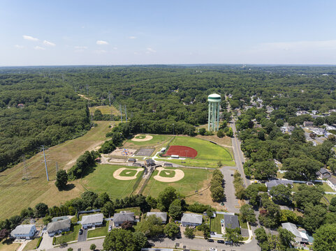 Aerial view of baseball fields and a water tower surrounded by lush green trees and suburban houses in Commack, New York, United States.