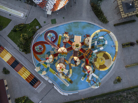 Aerial view of a colorful water park with twisting slides, a central pool, and palm tree decorations in Bulgaria.