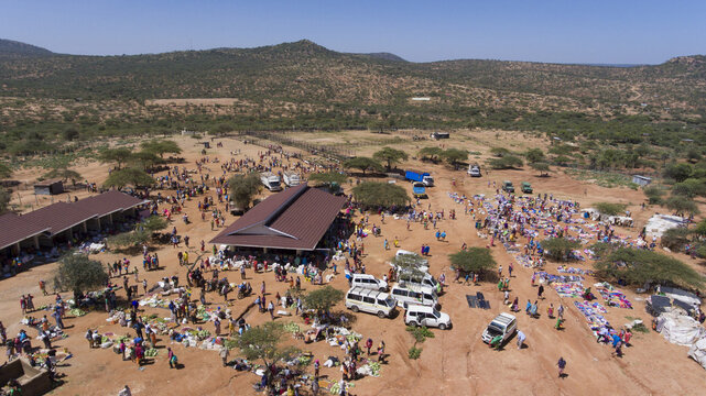 Aerial view of a bustling outdoor market in Oldonyiro with people trading goods, parked vehicles, and simple stalls set against a dry landscape in Oldonyiro, Isiolo County, Kenya.