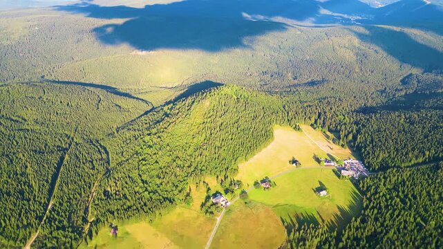 Aerial view of Bukovec Hill and Jizerka Village surrounded by dense pine forests and green meadows in Korenov, Liberec Region, Czechia.