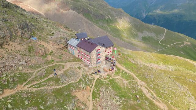 Aerial view of the Breslauer Hutte mountain refuge with hikers on the terrace surrounded by the rocky slopes of the Otztaler Alps in Vent, Tirol, Austria.