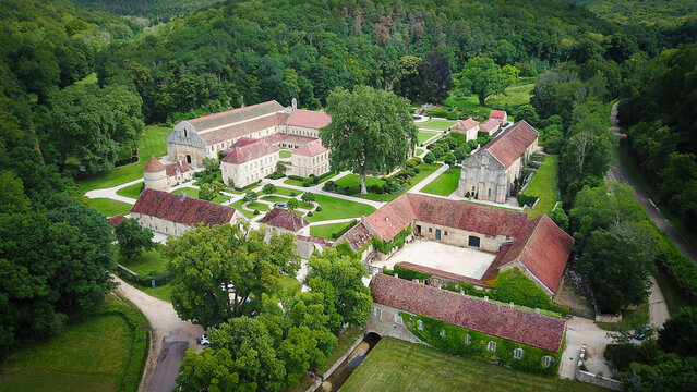 Aerial view of Fontenay Abbey with its historic stone buildings, red-tiled roofs, and manicured gardens surrounded by lush forest in Montbard, Bourgogne-Franche-Comte, France.