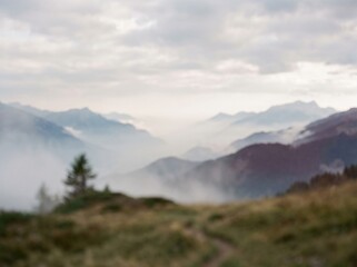 Fototapeta premium Breathtaking view of the misty alps in autumn, with a winding hiking trail leading through the golden grass in the foreground and layers of mountains in the distance