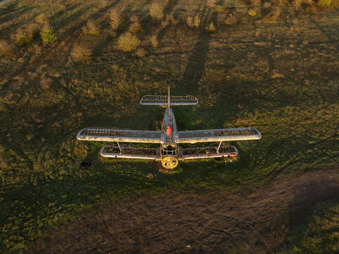 Aerial view of an abandoned biplane resting in a grassy field with a person in an orange jacket standing on the fuselage during golden hour in Bulgaria.