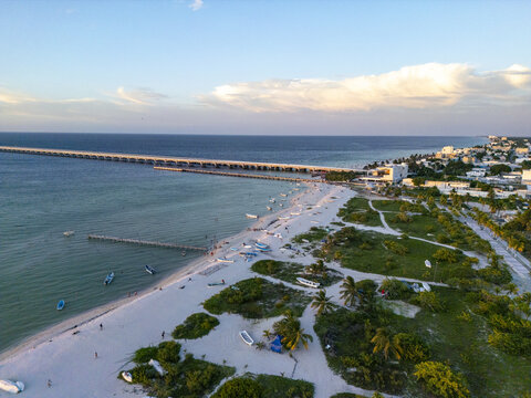 Aerial view of Playa Puerto Progreso with its long pier extending into the turquoise sea, white sandy beach, small boats, and lush coastal vegetation in Yucatan, Mexico.