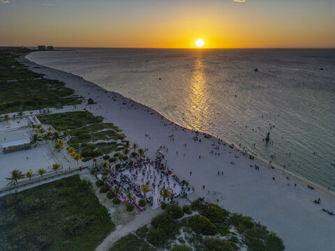 Aerial view of Playa Puerto Progreso at sunset with people gathered on a beach platform, calm ocean waves, and golden hour light reflecting on the water in Yucatan, Mexico.