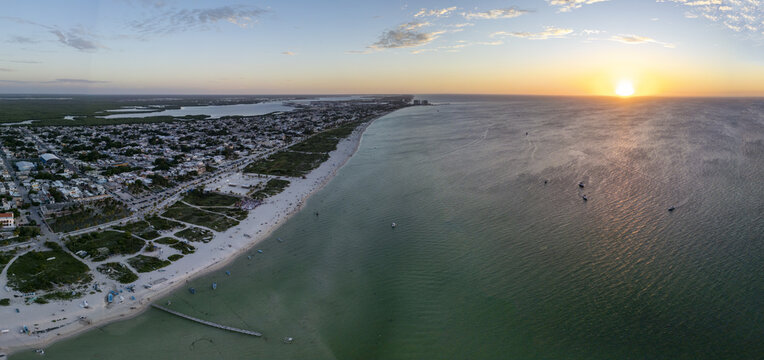 Aerial view of Playa Puerto Progreso at sunset, featuring the sandy coastline, calm turquoise waters, and the town infrastructure under a golden sky in Yucatan, Mexico.