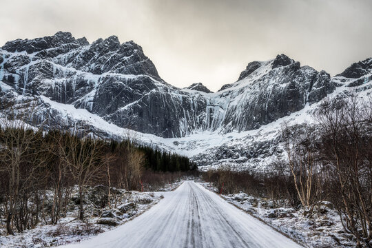 View of a snow-covered road leading towards the dramatic mountains of Lofoten in Nordland, Norway.