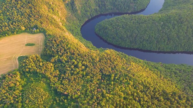 Aerial view of Solenicka podkova meander on the Vltava river surrounded by dense forest and agricultural fields during golden hour in Zduchovice, Central Bohemian Region, Czechia.