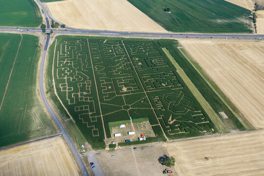 Aerial view of a large corn maze with intricate paths and patterns cut into the field, surrounded by agricultural land and a road in Soultz-Haut-Rhin, Grand Est, France.