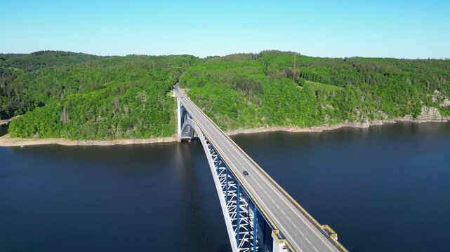 Aerial view of the Zdakov Bridge spanning the Vltava River, surrounded by lush green forests and calm water in Orlik nad Vltavou, South Bohemian Region, Czechia.