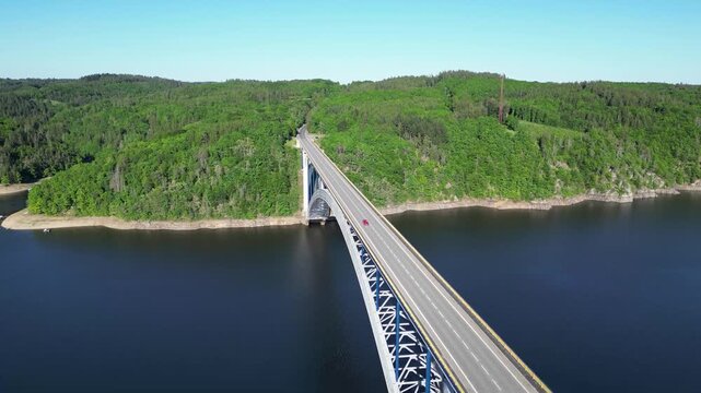 Aerial view of the iconic Zdakov Bridge spanning the Vltava River, surrounded by lush green forests in Orlik nad Vltavou, South Bohemian Region, Czechia.