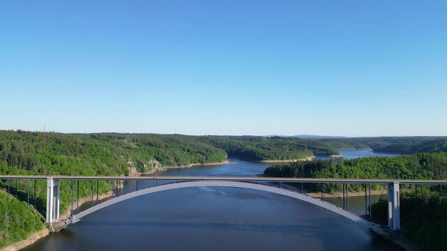 Aerial view of Zakov Bridge spanning the Vltava River reservoir, surrounded by dense green forests in Orlik nad Vltavou, South Bohemian Region, Czechia.
