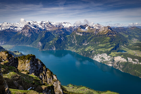 View of Stoos overlooking the deep blue waters of Lake Lucerne surrounded by snow-capped Alpine peaks and lush green slopes in Schwyz, Schwyz, Switzerland.