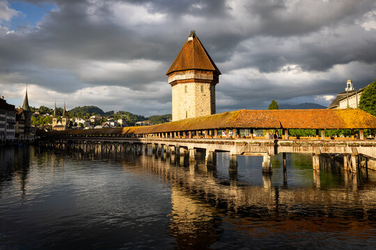View of the historic wooden Chapel Bridge and its octagonal water tower spanning the Reuss River under a dramatic cloudy sky in Lucerne, Lucerne, Switzerland.