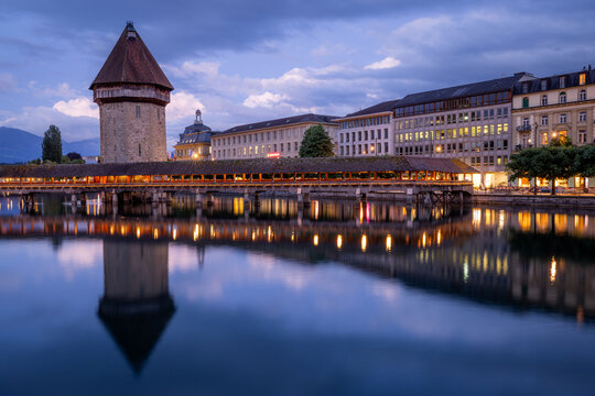 View of the historic Chapel Bridge spanning the Reuss River with illuminated buildings and reflections on the water in Lucerne, Lucerne, Switzerland.