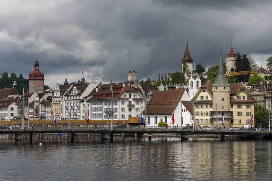 View of the historic Chapel Bridge and traditional architecture along the Reuss River under a dramatic cloudy sky in Lucerne, Lucerne, Switzerland.